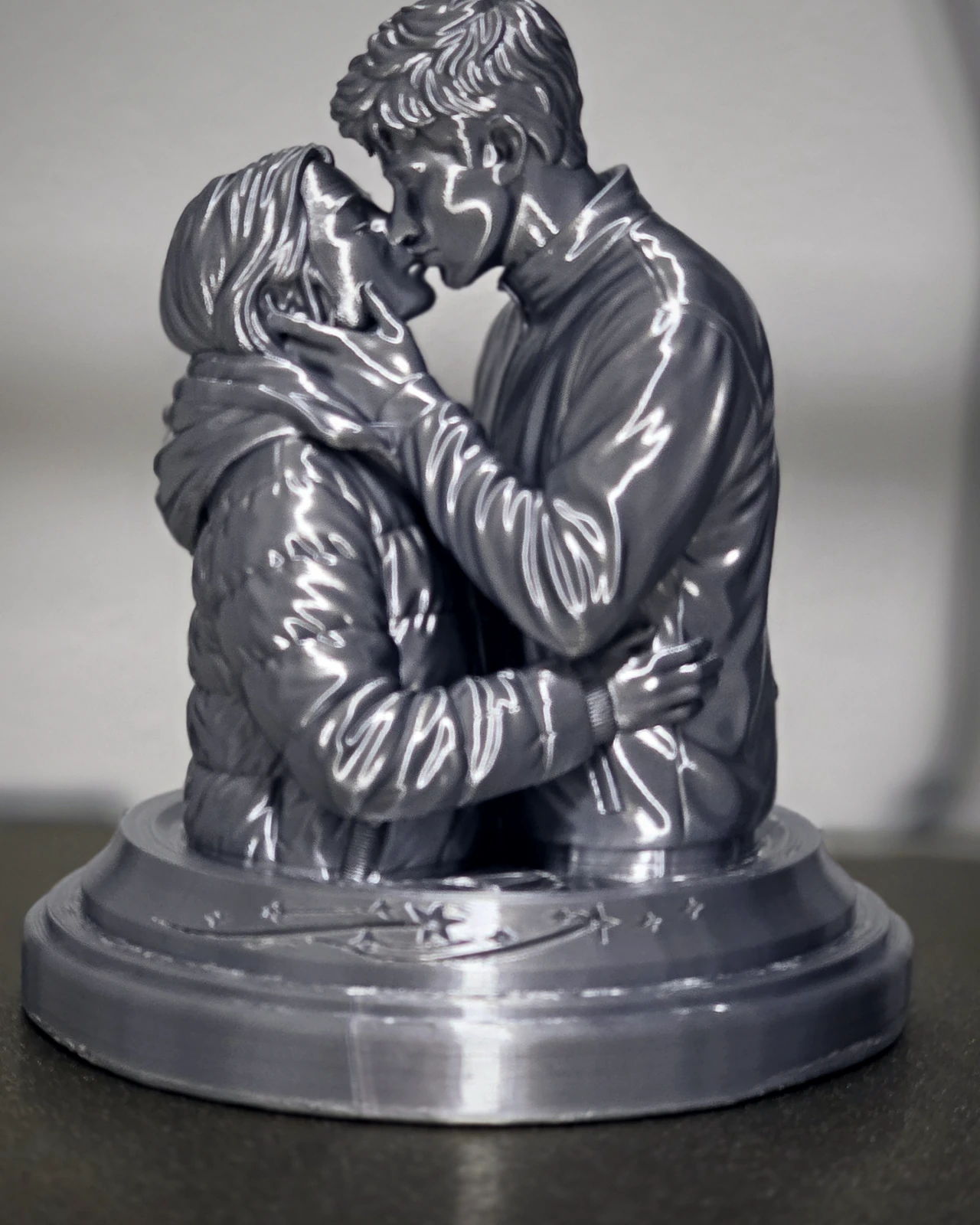 Escultura prateada de um casal se beijando, sobre base redonda com estrelas gravadas